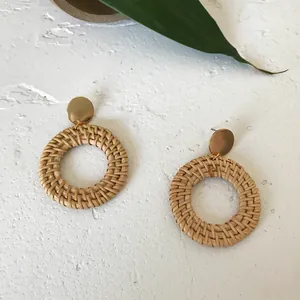 Macro view of bohemian round woven rattan earrings with a golden stud on stone surface