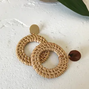 Close-up of bohemian round rattan drop earrings with gold studs on a stone surface
