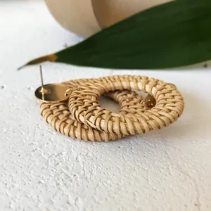 Close-up of bohemian rattan hoop earrings with gold metal studs on a white surface