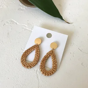 Bohemian rattan teardrop earrings with golden studs on a white display card with greenery