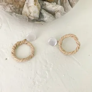 Close-up of geometric rattan hoop earrings with white resin studs on a textured background