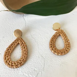 Handmade rattan teardrop earrings with golden metal studs on a natural stone background