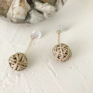 Close-up of elegant straw woven ball earrings with gold-plated rods on natural stone surface