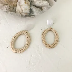 Detailed view of handmade rattan drop earrings with white resin studs on a textured background