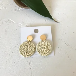 Detail of bohemian rattan drop earrings with golden studs on white display card