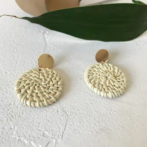 Bohemian round rattan drop earrings with gold metal studs on a white stone background