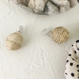 Detail of handmade woven rattan drop earrings with white resin studs and gold hardware