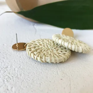 Macro detail of geometric woven rattan hoop earrings with gold studs on stone base
