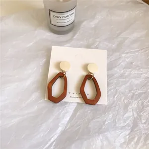 Close-up of geometric wood and white resin drop earrings on a square display card