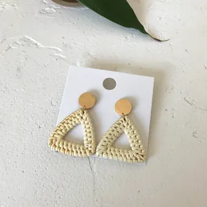 Detail of bohemian triangular woven rattan earrings with golden metallic studs on white stone