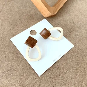 Detail view of geometric wooden stud earrings with teardrop links on white display card