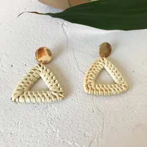 Close-up of bohemian woven triangular rattan earrings with golden round metallic stud detail