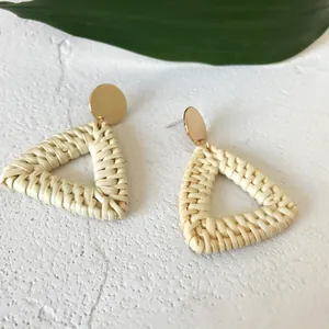 Close-up of bohemian hollow triangle rattan earrings with golden metal stud details