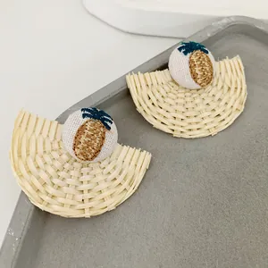 Auffällige geflochtene Fächer-Ohrringe mit Ananas-Stickerei auf beigem Holzgrund