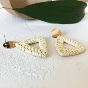 Macro shot of handmade triangular woven straw earrings with gold metal stud detail