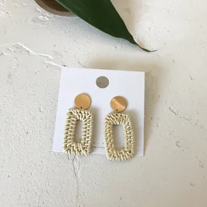Close-up of bohemian rectangle rattan earrings with golden studs on a white display card
