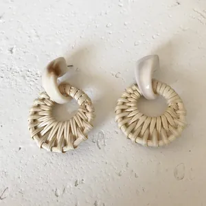 Bohemian woven rattan earrings with cream resin top on a textured stone surface