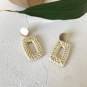 Detail of woven rattan earrings with golden studs on a natural stone background
