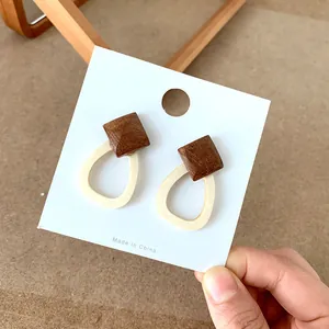 Detail view of vintage geometric wooden earrings with cream teardrop hoop on a display card