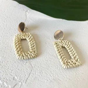 Detail of cream woven rattan rectangle drop earrings with gold circular studs and leaf