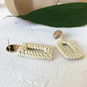 Macro shot of rectangular straw earrings with gold metal studs on a white texture