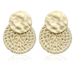 Detail of bohemian rattan earrings with textured gold metal disc and woven cream straw