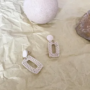 Bohemian geometric woven rattan hoop earrings with white round studs on a natural stone background