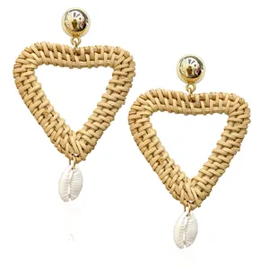 Detailed close-up of handmade heart-shaped rattan earrings with golden studs and shell accents