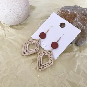 Detail view of bohemian rattan earrings with red discs on warm textured background