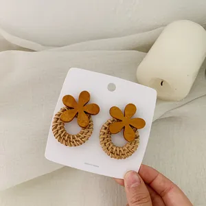 Detailed view of bohemian woven rattan earrings with dark brown wooden flower accents