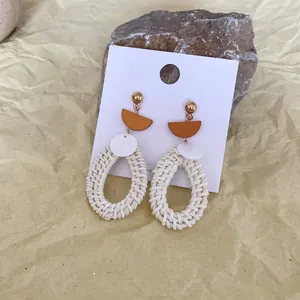 Macro view of bohemian woven rattan teardrop earrings with golden studs on natural stone