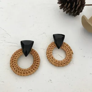 Detail of bohemian rattan earrings with black triangle studs on a textured stone surface