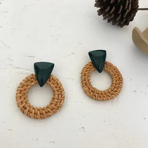 Detail of bohemian rattan earrings with dark green resin triangles on white surface