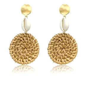 Detailed view of woven rattan earrings featuring gold discs and natural shells