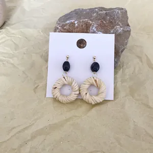 Detail of bohemian woven straw earrings with black beads on a natural stone background