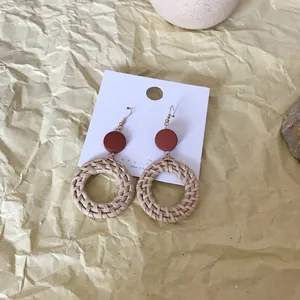 Close-up of woven rattan hoop earrings with reddish-brown top on a textured background