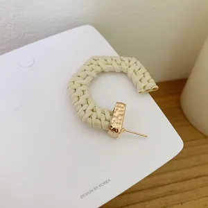 Detail of C-shaped beige raffia woven earrings with gold-toned metal ends and stud pins