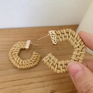 Close-up of handmade Bohemian C-shaped woven rattan earrings with gold metal fasteners
