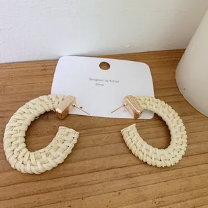Detailed macro view of bohemian hand-woven cream rattan hoop earrings with gold metal accents