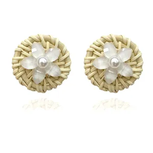 Detail of round woven rattan earrings featuring white floral petals and pearl centers
