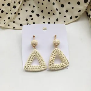 Detailed view of cream woven rattan earrings with geometric triangular drop design