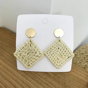 Bohemian geometric straw woven earrings with golden metal studs on a wooden background