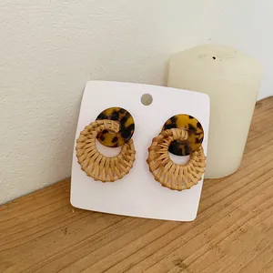 Detail of woven rattan hoop earrings with tortoiseshell studs on display card with candle