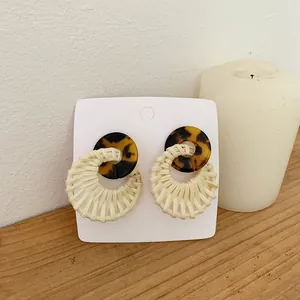 Bohemian rattan woven hoop earrings with dark tortoise shell resin rings on a display card