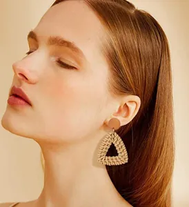 Close-up of bohemian rattan woven triangular earrings worn by a model in warm light