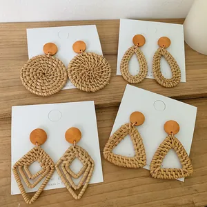 Macro view of four geometric woven rattan earrings with orange wood studs on a wooden surface