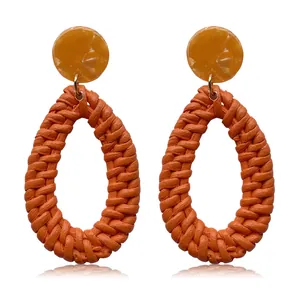Close-up of bohemian earrings with amber resin studs and orange rattan teardrop pendants