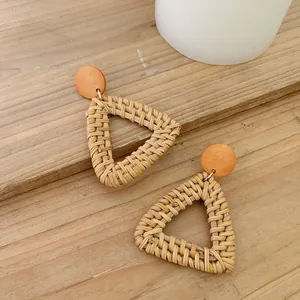 Detail of handmade triangular rattan earrings with wooden studs on a light wood background