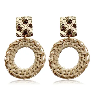 Detail of woven rattan earrings with hammered gold metal rectangular studs on white background