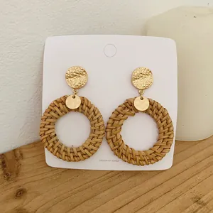 Detail of round hollow woven rattan earrings with hammered gold metal on a wooden surface